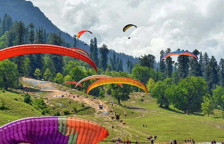 Colourful paragliders soar above lush green valleys and rivers, Manali's best adventure sport.