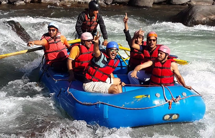 Group of adventurers rafting through white waters of Beas River surrounded by Kullu's mountain scenery
